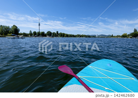 Turquoise paddleboard with a purple paddle on board in the Danube River illustrate summer water sport and mental vitality. Turquoise paddleboard with a purple paddle on board in the Danube River illustrate summer water sport and mental vitality. 142462680
