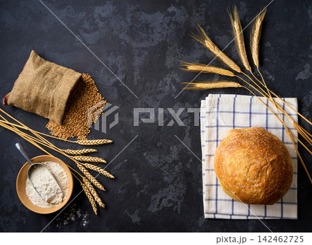 Round loaf of wheat rustic bread with sourdough on dark kitchen table with flour and ears of wheat.Top view. Round loaf of wheat rustic bread with sourdough on dark kitchen table with flour and ears of wheat.Top view. 142462725
