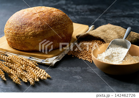 Whole grain loaf of the wheat sourdough bread hearth  on dark kitchen table with flour and ears of wheat. 142462726
