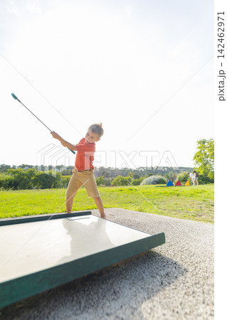 Young boy playing mini golf swinging club outdoors 142462971