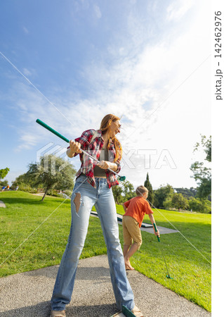 Woman and son playing mini golf outdoors Woman and son playing mini golf outdoors 142462976