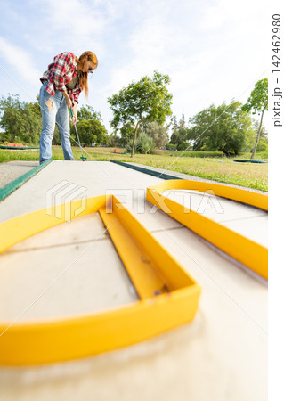 Woman playing miniature golf on outdoor course Woman playing miniature golf on outdoor course 142462980