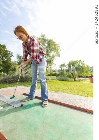 Woman playing mini golf on an outdoor course Woman playing mini golf on an outdoor course 142462991