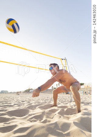 Man plays volleyball on the beach during a sunny day with clear skies and a volleyball net in the background Man plays volleyball on the beach during a sunny day with clear skies and a volleyball net in the background 142463010