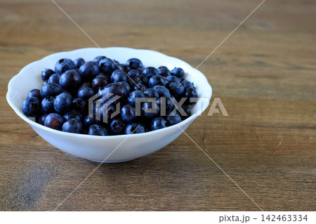 Fresh Blueberries and Bilberries in White Ceramic Bowl on Wooden Table. Space for text Fresh Blueberries and Bilberries in White Ceramic Bowl on Wooden Table. Space for text 142463334