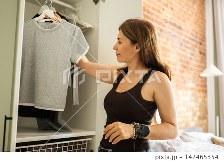 Woman Hanging Freshly Ironed Clothes In A Wardrobe In A Light Room At Home Woman Hanging Freshly Ironed Clothes In A Wardrobe In A Light Room At Home 142465354