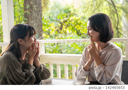 木立のカフェで笑顔でおしゃべりする女友達 木立のカフェで笑顔でおしゃべりする女友達 142465653