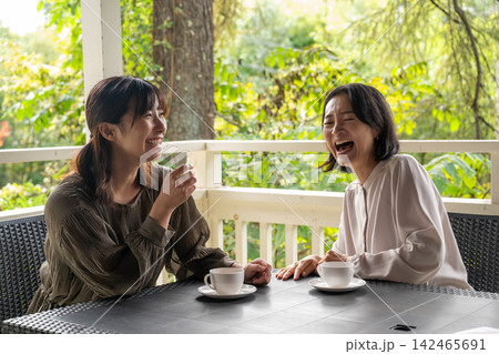 別荘地のテラスでコーヒー片手に会話を楽しむ女性 別荘地のテラスでコーヒー片手に会話を楽しむ女性 142465691