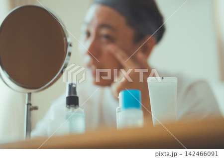 コスメが並ぶ卓上ミラーの前でスキンケアをする40代男性のメンズケア コスメが並ぶ卓上ミラーの前でスキンケアをする40代男性のメンズケア 142466091