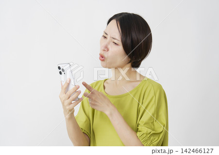 スマホを見て怒るミドル女性　白背景 142466127