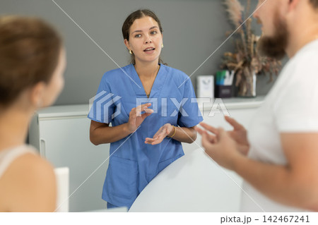 Dental clinic administrator talks to patients at reception desk 142467241