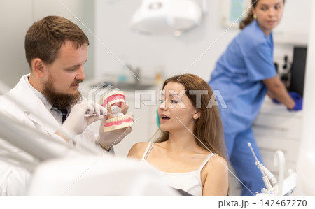 Male dentist shows a client a model of teeth in the office Male dentist shows a client a model of teeth in the office 142467270