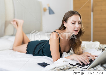 Woman in pajamas on bed with laptop 142467381