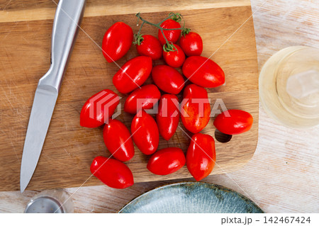 Pile of red cherry plum tomatoes on wooden cutting board Pile of red cherry plum tomatoes on wooden cutting board 142467424