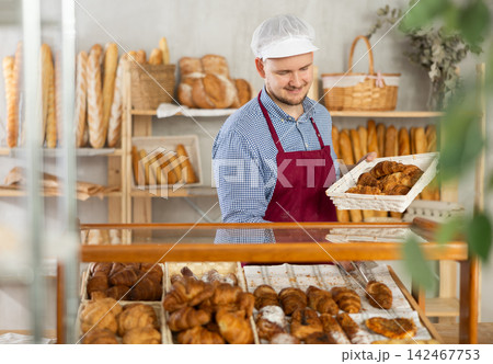 Selling fresh croissants in bakery - Baker places hot croissants on display Selling fresh croissants in bakery - Baker places hot croissants on display 142467753