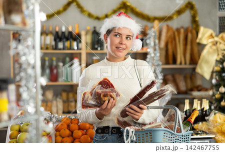 Female customer with a cart of groceries buys dried sausage and ham in supermarket - - prepares to celebrate Christmas 142467755