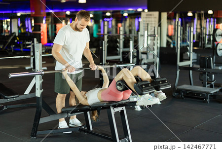 Girl does barbell exercises, and asks guy friend to insure her during exercises. 142467771