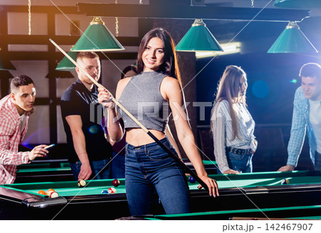 Young woman playing in billiard. Posing near the table with a cue in her hands Young woman playing in billiard. Posing near the table with a cue in her hands 142467907