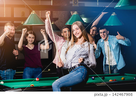 Young woman playing in billiard. Posing near the table with a cue in her hands Young woman playing in billiard. Posing near the table with a cue in her hands 142467908