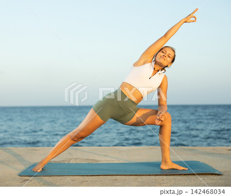 Sportive girl practicing triangle pose of yoga on seashore Sportive girl practicing triangle pose of yoga on seashore 142468034