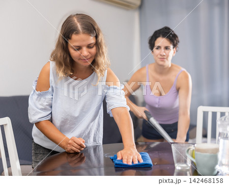 Young female couple cleaning living room together Young female couple cleaning living room together 142468158