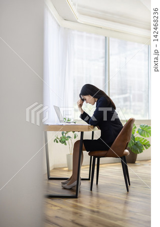 窓辺のデスクで額に手を当てて俯く若い日本人のビジネスウーマン 窓辺のデスクで額に手を当てて俯く若い日本人のビジネスウーマン 142468236