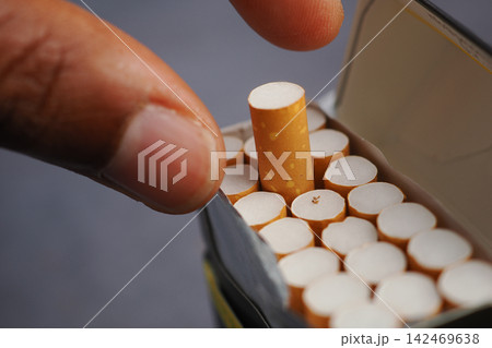 Cigarette being taken from a pack by a hand Cigarette being taken from a pack by a hand 142469638