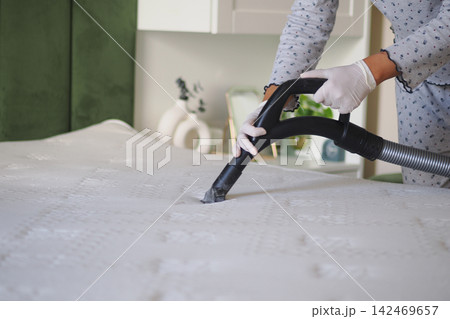 A woman is using a vacuum cleaner on a mattress in a bedroom. 142469657