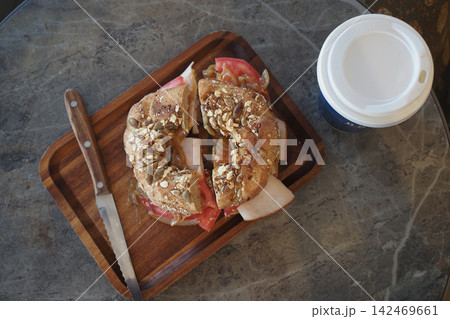 a cut bagel sandwich with seeds on a wooden tray next to a knife and a coffee cup a cut bagel sandwich with seeds on a wooden tray next to a knife and a coffee cup 142469661
