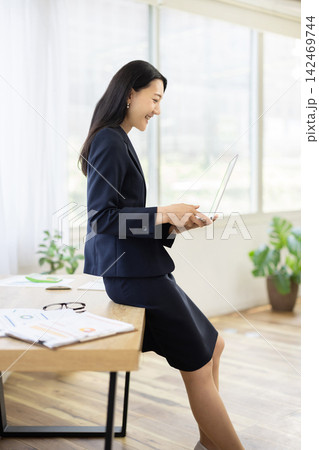 明るい窓辺のデスク脇でノートパソコンを操作する若い日本人のビジネスウーマン 明るい窓辺のデスク脇でノートパソコンを操作する若い日本人のビジネスウーマン 142469744