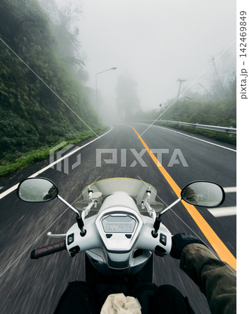 POV shot of riding a scooter on a wet, winding mountain road through a dense, foggy forest. POV shot of riding a scooter on a wet, winding mountain road through a dense, foggy forest. 142469849