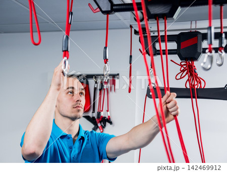 Physiotherapy. Suspension training therapy. Young man doing fitness traction therapy with suspension-based exercise training system. 142469912