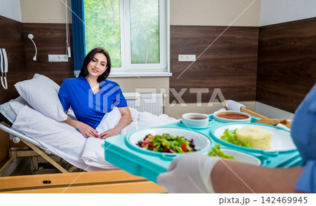 Nurse in medical coat is holding a tray with breakfast for the young female patient. Nurse in medical coat is holding a tray with breakfast for the young female patient. 142469945