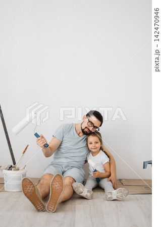 A father and his young daughter sit on the floor, smiling and holding paint rollers, ready to redecorate their home A father and his young daughter sit on the floor, smiling and holding paint rollers, ready to redecorate their home 142470946
