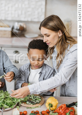A mother and her children are preparing a fresh salad with various vegetables in a bright, modern kitchen A mother and her children are preparing a fresh salad with various vegetables in a bright, modern kitchen 142471132