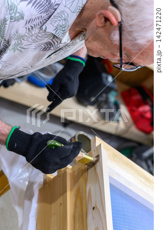 Elderly man applying varnish coat to a wooden box with a brush. Male carpenter working on a DIY craft project at a workbench in a workshop 142471220