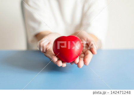 Close up of hands holding red heart on blue background for charity and healthcare concept 142471248