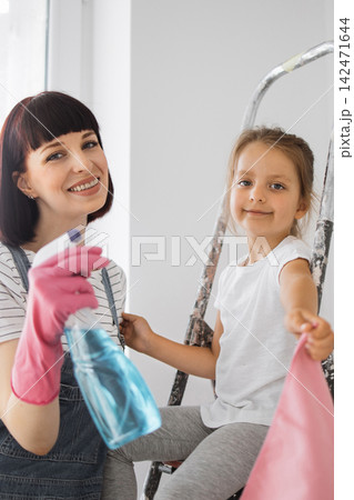 A smiling mother and her young daughter are on a ladder, preparing to clean a room, holding cleaning supplies and cloths A smiling mother and her young daughter are on a ladder, preparing to clean a room, holding cleaning supplies and cloths 142471644