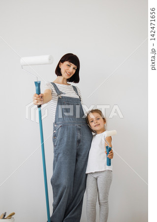 A woman and a young girl in overalls stand side-by-side holding paint rollers, ready to redecorate a room A woman and a young girl in overalls stand side-by-side holding paint rollers, ready to redecorate a room 142471656