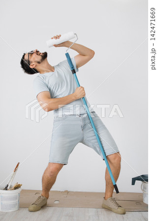 A man playfully holds a paint roller to his mouth as if singing into a microphone, embodying a moment of joy during home renovation 142471669