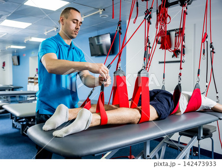 Physiotherapy. Suspension training therapy. Young man doing fitness traction therapy with suspension-based exercise training system. Physiotherapy. Suspension training therapy. Young man doing fitness traction therapy with suspension-based exercise training system. 142473933