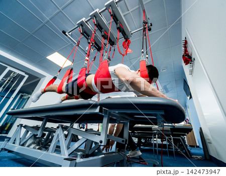 Physiotherapy. Suspension training therapy. Young man doing fitness traction therapy with suspension-based exercise training system. Physiotherapy. Suspension training therapy. Young man doing fitness traction therapy with suspension-based exercise training system. 142473947