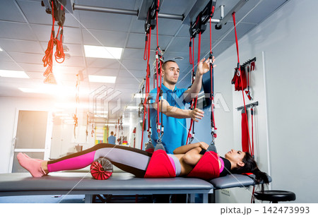 Physiotherapy. Suspension training therapy. Young woman doing fitness traction therapy with suspension-based exercise training system. Physiotherapy. Suspension training therapy. Young woman doing fitness traction therapy with suspension-based exercise training system. 142473993