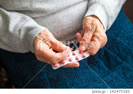 Senior hands holding medication blister pack with pink pill, elderly healthcare and medication management Senior hands holding medication blister pack with pink pill, elderly healthcare and medication management 142475193