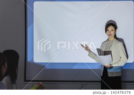 スクリーン横で手を差し出し説明する女性ビジネスパーソン 142476379