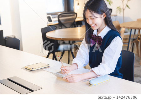 スマートフォンを見ながらノートをとる女子高校生 スマートフォンを見ながらノートをとる女子高校生 142476506