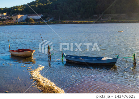 Traditional vintage wooden fishing boats moored in the calm lagoon of Etang de Gruissan with a soft pinkish hue on the water surface in Occitanie, South of France Traditional vintage wooden fishing boats moored in the calm lagoon of Etang de Gruissan with a soft pinkish hue on the water surface in Occitanie, South of France 142476625