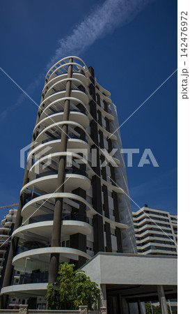 Low angle view of a modern residential building with curved white balconies and a blue sky Low angle view of a modern residential building with curved white balconies and a blue sky 142476972