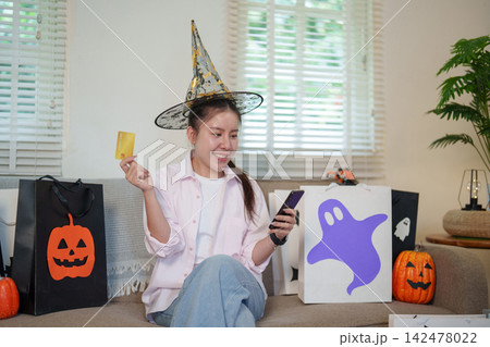 Asian woman wearing witch hat using credit card and smartphone for Halloween online shopping 142478022