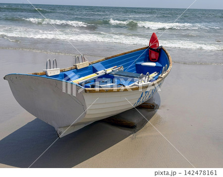Lifeguards Row Boat Sits on Sand at Beach Near Waves and Ocean Lifeguards Row Boat Sits on Sand at Beach Near Waves and Ocean 142478161